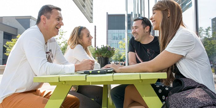 picture of centennial college students sitting at a picnic table in the progress campus courtyard
